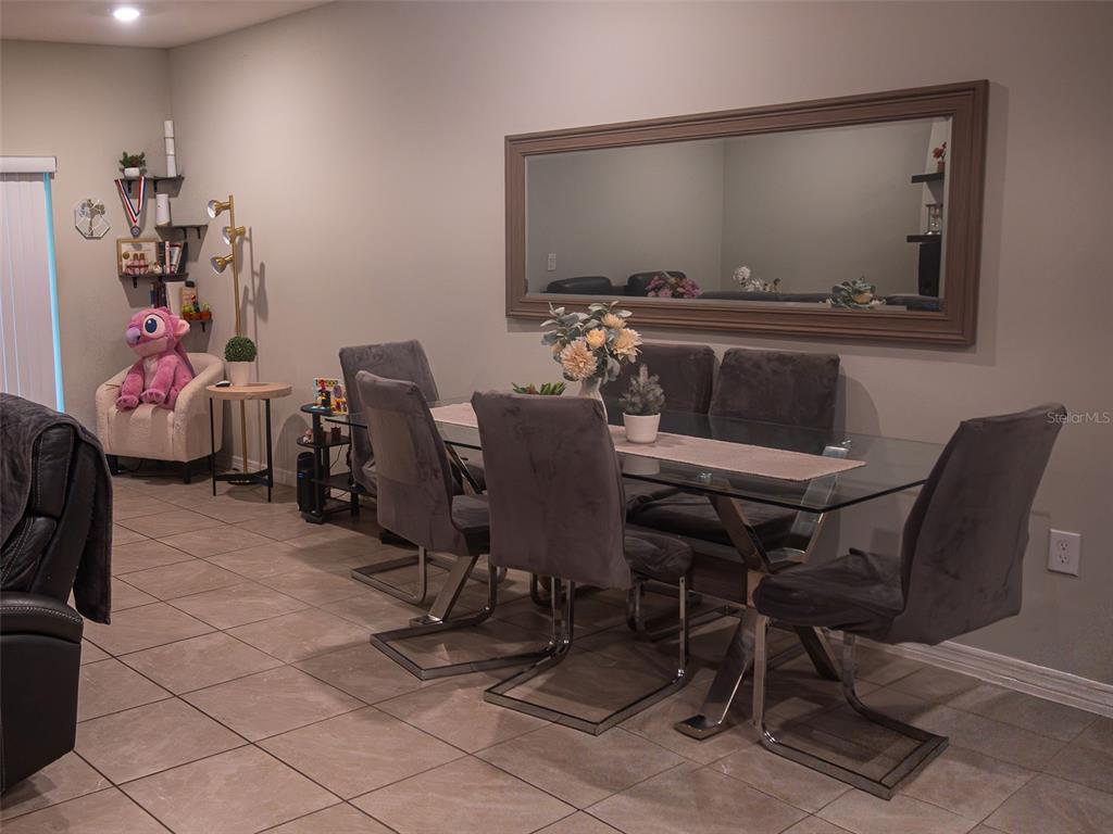 A dining room features a glass-top table with grey upholstered chairs and a large mirror — 4878 CORAL CASTLE DRIVE, KISSIMMEE, FL