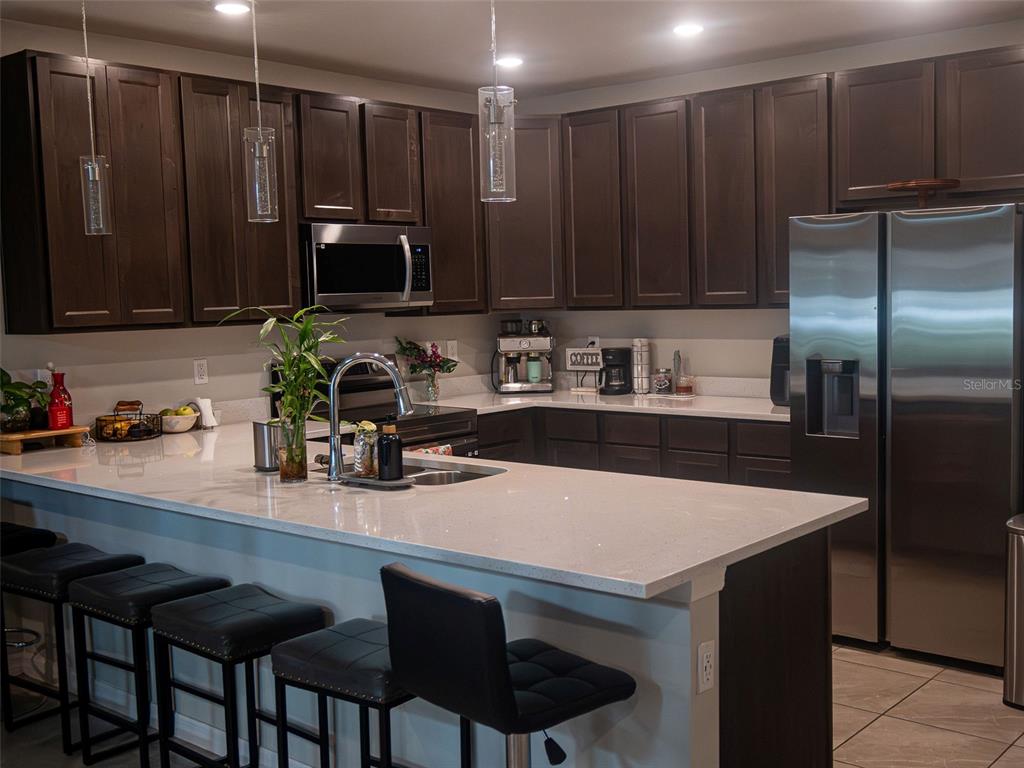 A kitchen features dark wood cabinets, a large white quartz island, and stainless steel appliances — 4878 CORAL CASTLE DRIVE, KISSIMMEE, FL