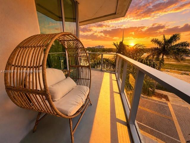 A wicker egg chair sits on a balcony overlooking a sunset view of palm trees — 2000 Metropica Way # 304, Sunrise FL 33323, SUNRISE, FL