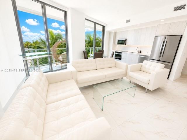A bright living room features white leather sofas, a glass coffee table, and an open kitchen — 2000 Metropica Way # 304, Sunrise FL 33323, SUNRISE, FL