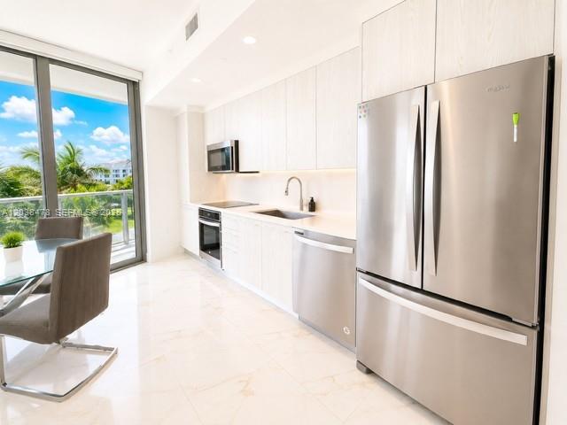 A modern kitchen features light wood cabinetry, stainless steel appliances, and a dining area — 2000 Metropica Way # 304, Sunrise FL 33323, SUNRISE, FL