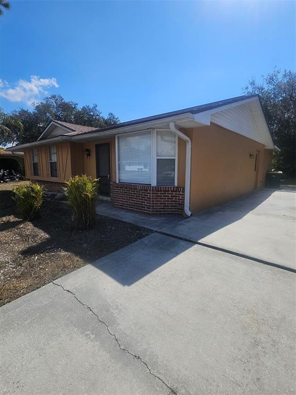 A single-story house with tan stucco walls, a brick base, and a concrete driveway — 1225 ARMSDALE AVENUE, PORT CHARLOTTE, FL