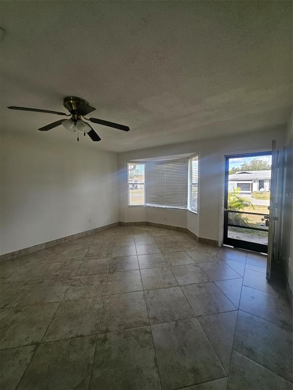An empty room features light-colored tile flooring, a ceiling fan, and a bay window — 1225 ARMSDALE AVENUE, PORT CHARLOTTE, FL
