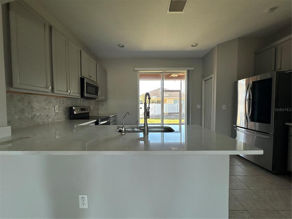 A kitchen features light gray cabinets, white quartz countertops, a center island, and stainless appliances — 6950 TOWERING SPRUCE DRIVE, RIVERVIEW, FL
