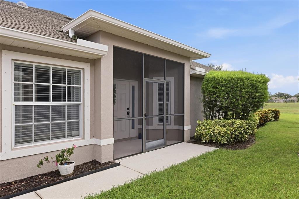 A tan house exterior features a screened-in entryway, a large window, and landscaped bushes — 3518 LAKEWOOD BOULEVARD, NORTH PORT, FL
