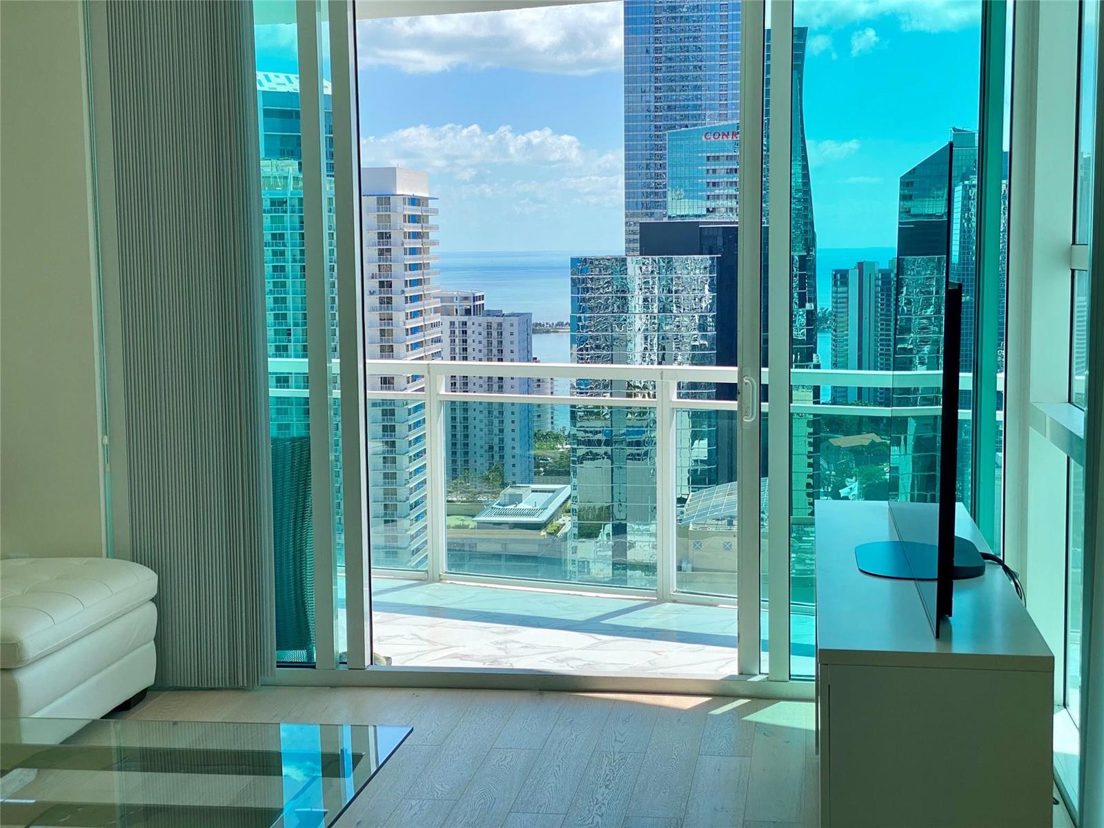 A living room with light wood floors overlooks a balcony and a city skyline view — 951 Brickell Avenue # 3611, Miami FL 33131, MIAMI, FL