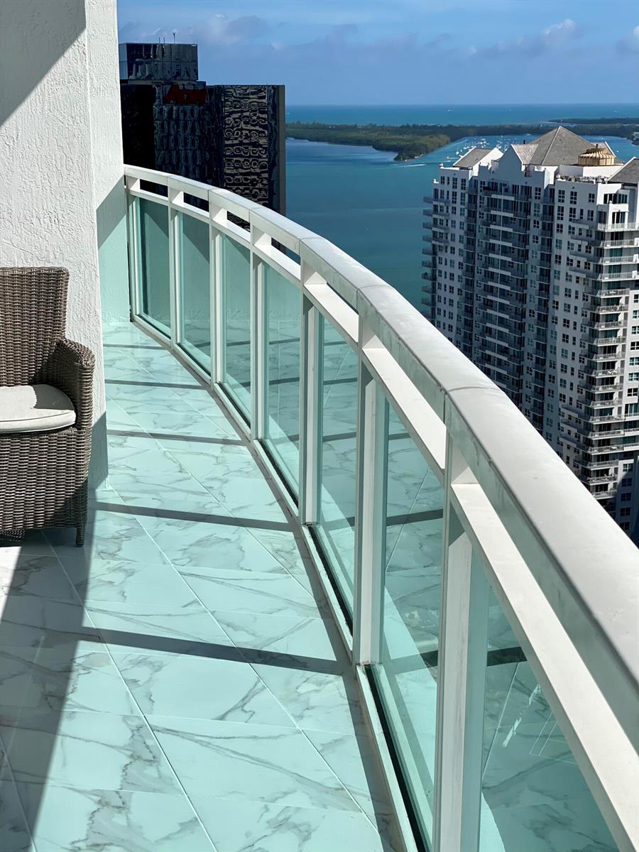 A balcony with marble-look tile flooring, a wicker chair, and glass railings overlooking the ocean — 951 Brickell Avenue # 3611, Miami FL 33131, MIAMI, FL