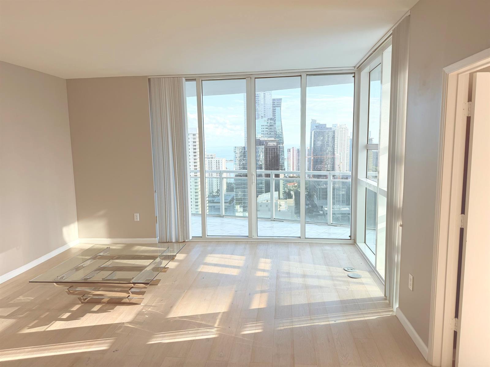 An empty living room with light wood floors, a glass coffee table, and floor-to-ceiling windows — 951 Brickell Avenue # 3611, Miami FL 33131, MIAMI, FL