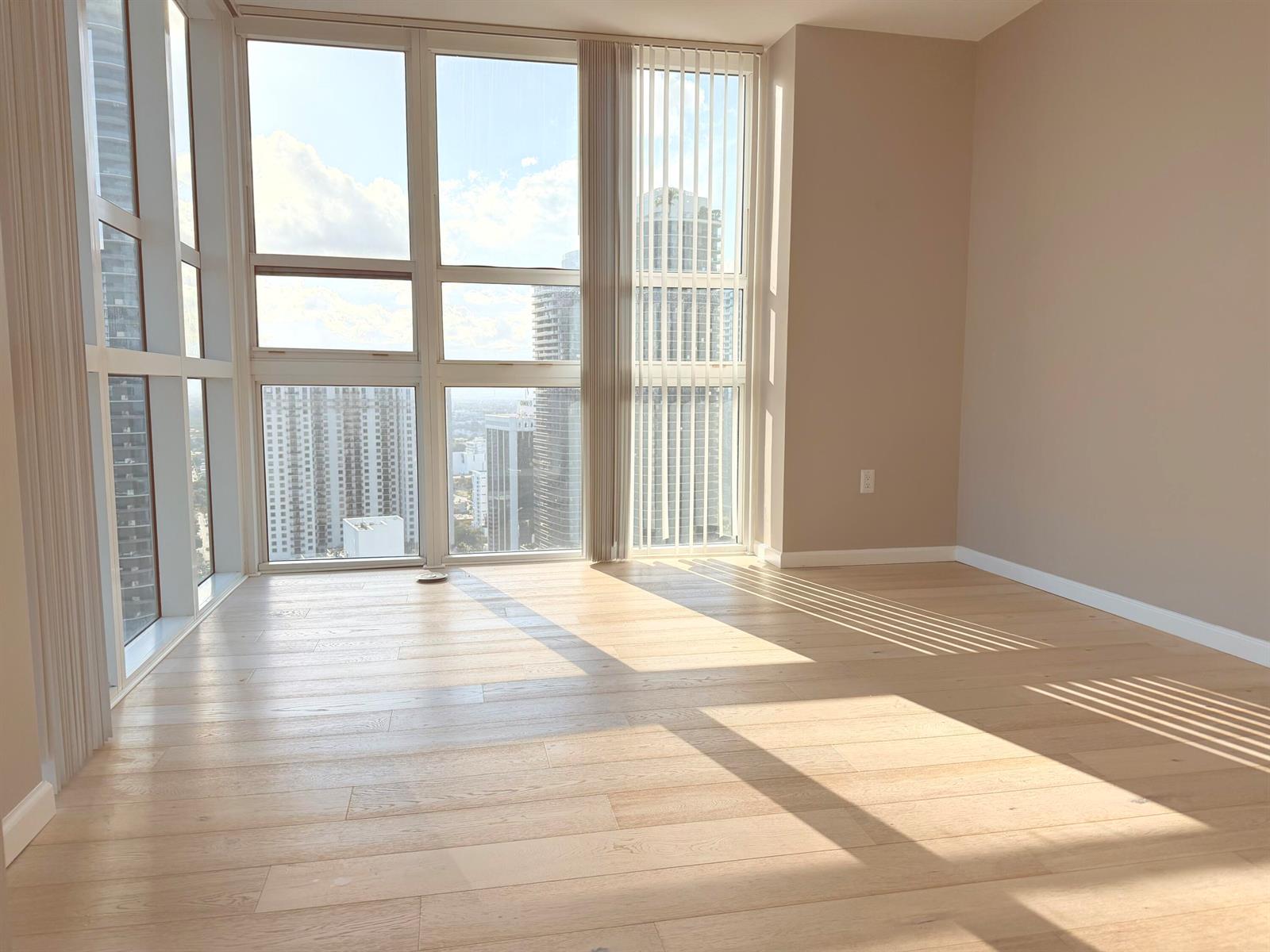 An empty room with light wood flooring, floor-to-ceiling windows, and city skyline views — 951 Brickell Avenue # 3611, Miami FL 33131, MIAMI, FL