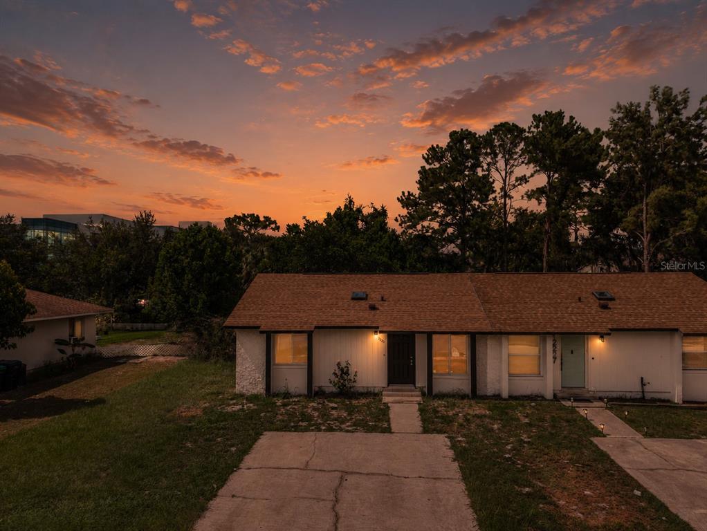 An exterior view of a single-story duplex at sunset with a concrete driveway and lawn — 12225 CORAL REEF DRIVE, ORLANDO, FL