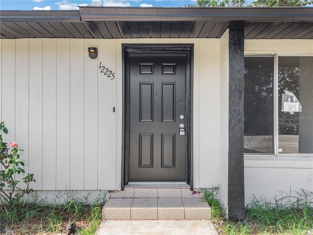 A black front door with a house number is centered on the exterior of a home — 12225 CORAL REEF DRIVE, ORLANDO, FL