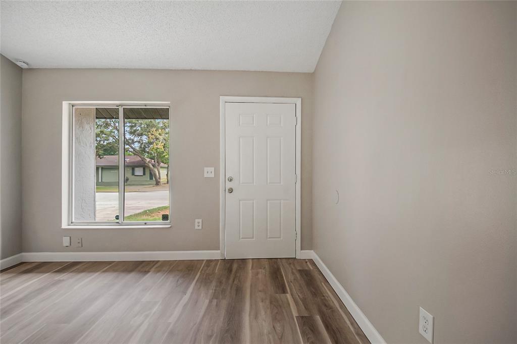 An interior room with light gray walls, wood-look flooring, a window, and a white door — 12225 CORAL REEF DRIVE, ORLANDO, FL