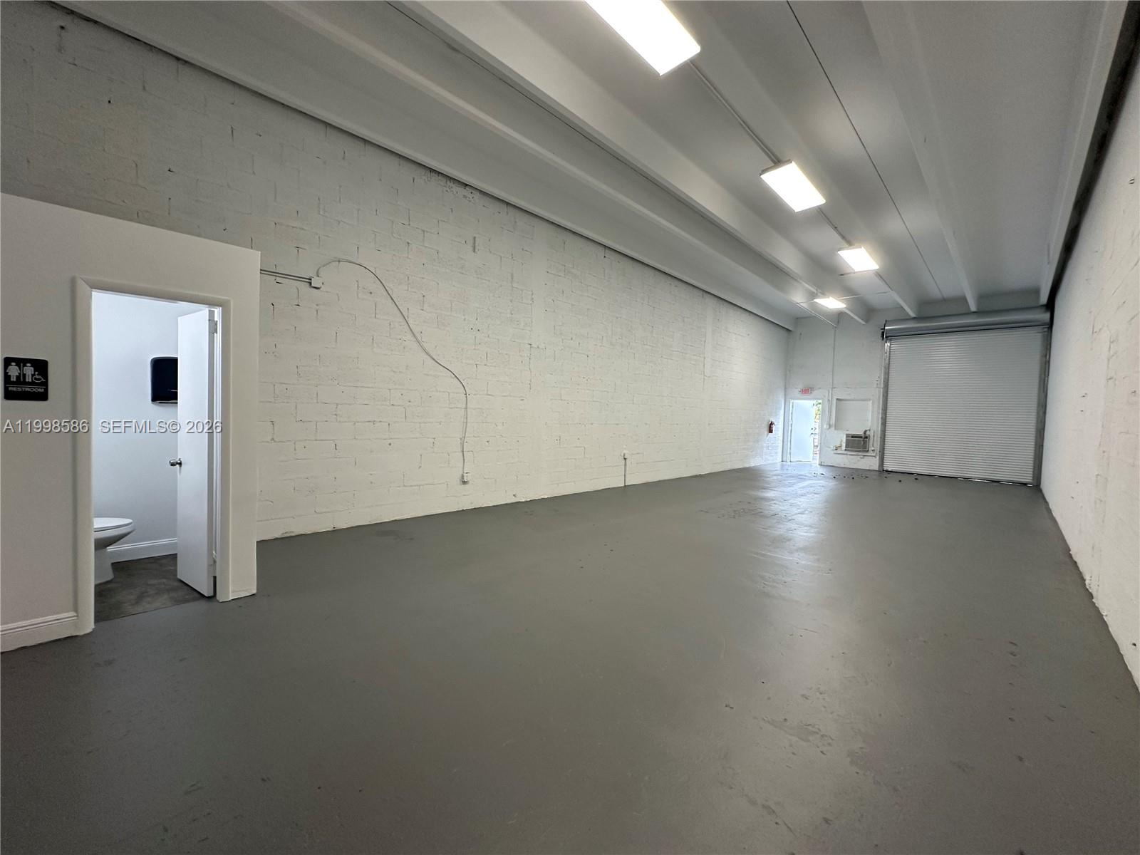 An empty industrial warehouse space features white painted brick walls, gray flooring, and a restroom — 5818 SW 25th St # 2, West Park FL 33023, WEST PARK, FL