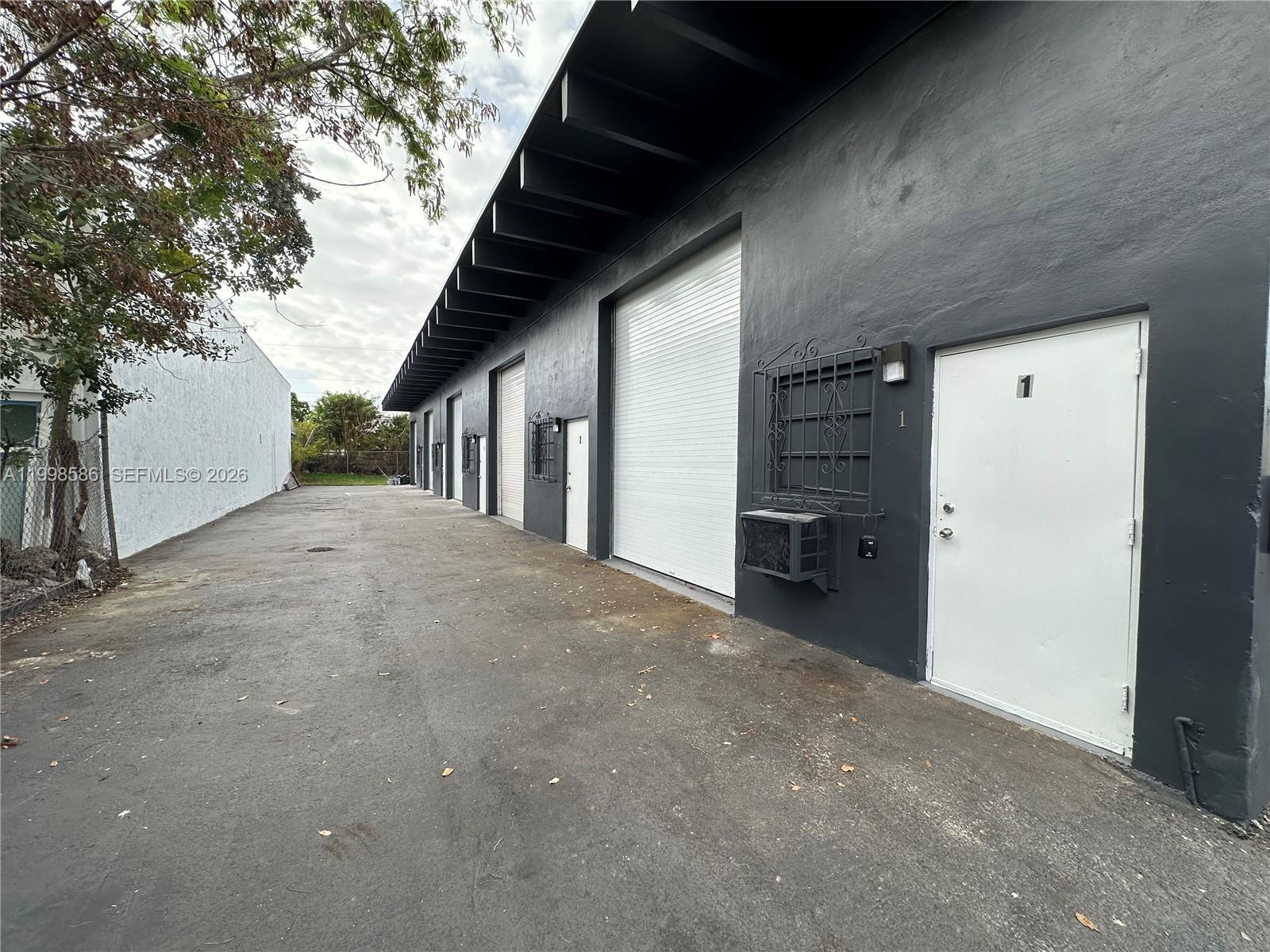 An exterior view of a dark gray industrial building with multiple roll-up doors and white entry doors — 5818 SW 25th St # 2, West Park FL 33023, WEST PARK, FL