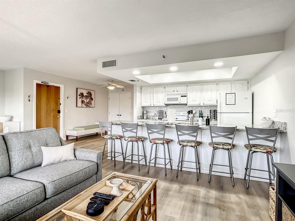 A living room with a gray sofa faces a kitchen featuring white cabinets and bar seating — 19727 GULF BOULEVARD UNIT G1, INDIAN ROCKS BEACH, FL