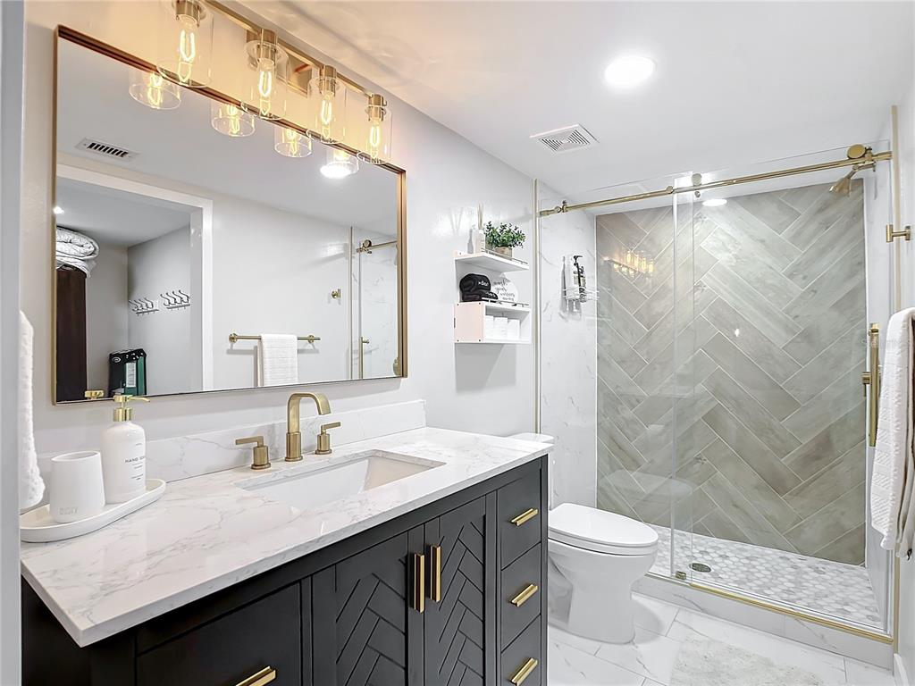A modern bathroom features a dark vanity with gold hardware, a marble countertop, and a shower — 19727 GULF BOULEVARD UNIT G1, INDIAN ROCKS BEACH, FL