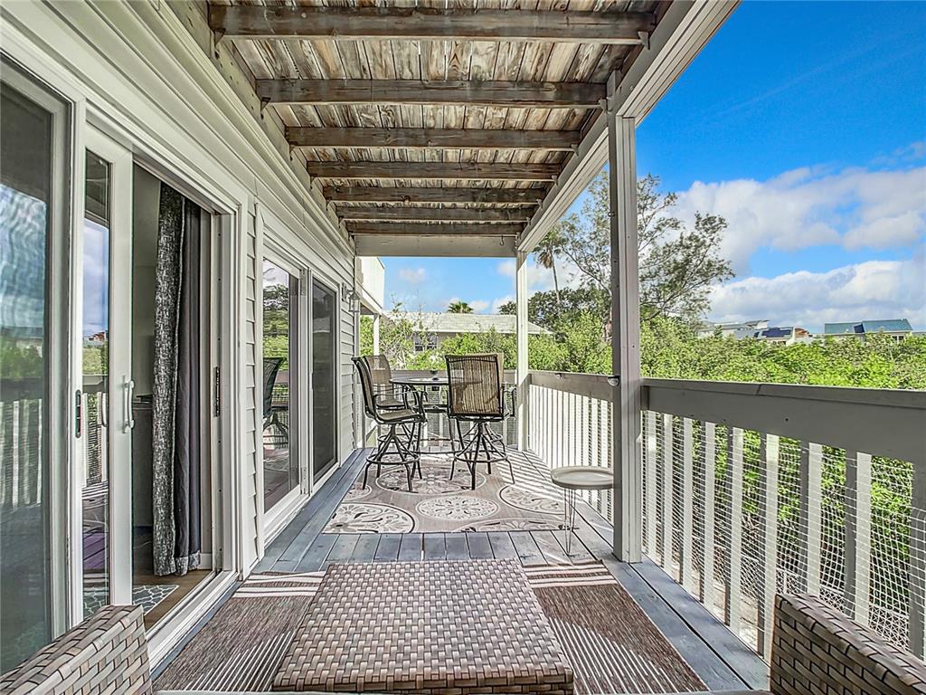 A covered wooden balcony features outdoor furniture, a patterned rug, and a white railing — 19727 GULF BOULEVARD UNIT G1, INDIAN ROCKS BEACH, FL