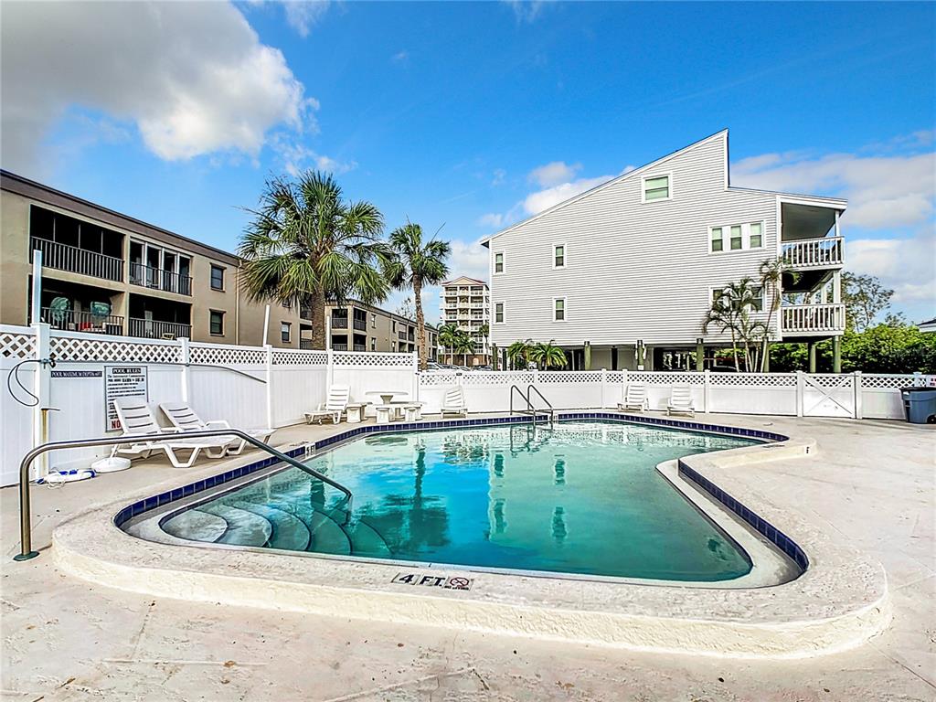 An outdoor swimming pool is surrounded by a white fence and multi-story apartment buildings — 19727 GULF BOULEVARD UNIT G1, INDIAN ROCKS BEACH, FL
