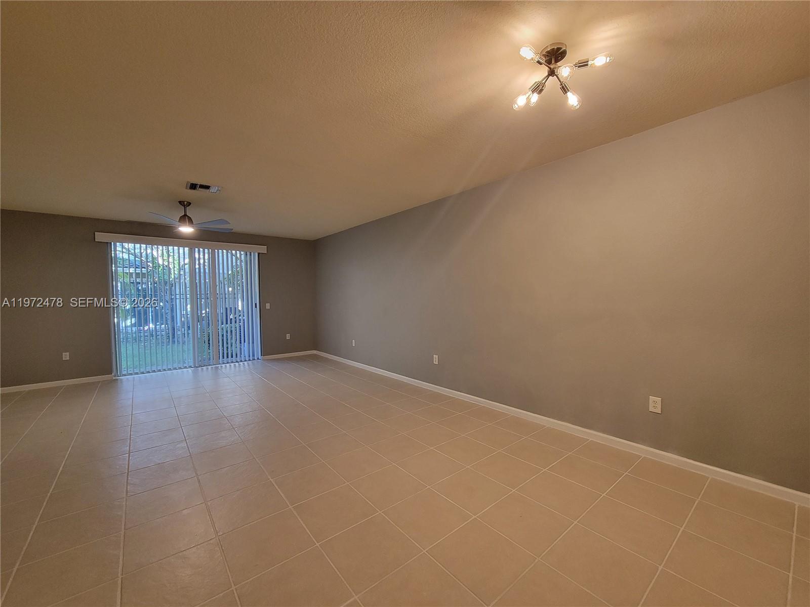 An empty living room features beige tile flooring, a ceiling fan, and sliding glass doors — 2761 SW 82nd Ave # 102, Miramar FL 33025, MIRAMAR, FL