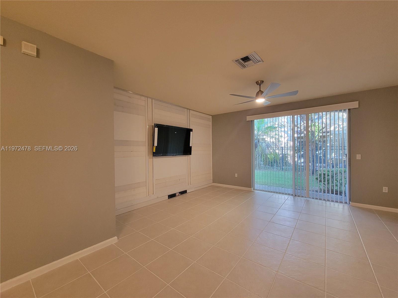 A living room features light tile flooring, a wall-mounted television, and sliding glass doors — 2761 SW 82nd Ave # 102, Miramar FL 33025, MIRAMAR, FL
