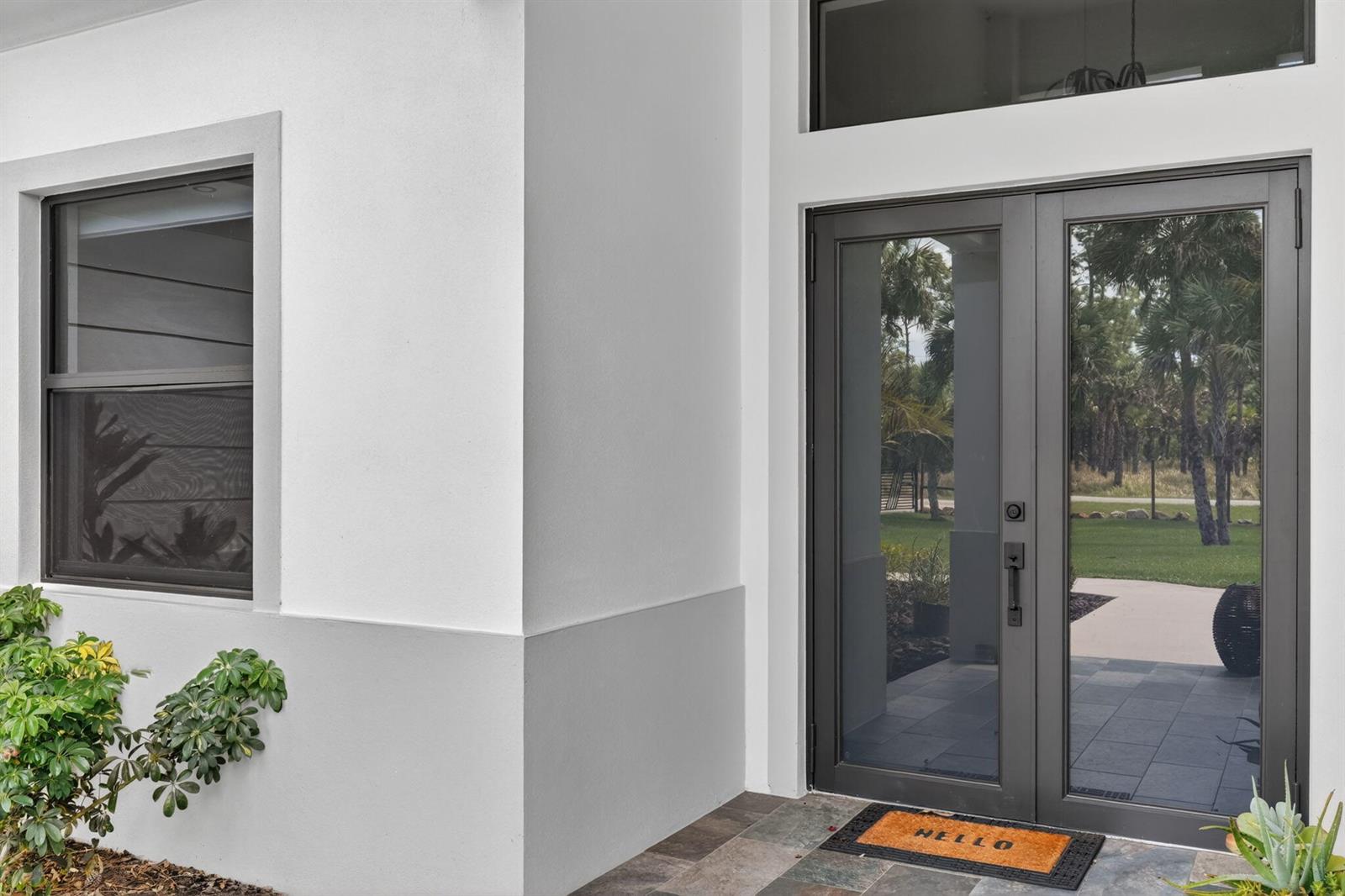 A modern home entrance features dark-framed glass double doors and a white exterior wall — 3263 SE 40th Ave Avenue SE, Naples FL 34117, NAPLES, FL