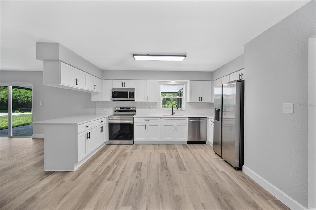 A modern kitchen features white cabinets, stainless steel appliances, and light wood-look flooring — 11033 SHERROUSE ROAD, LAKELAND, FL