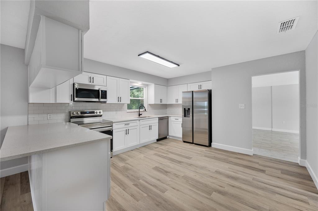 A kitchen with white cabinets, stainless steel appliances, light countertops, and wood-look flooring — 11033 SHERROUSE ROAD, LAKELAND, FL