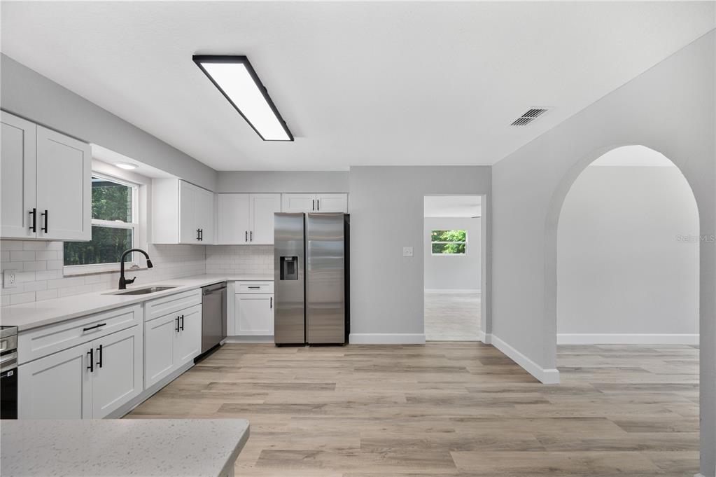 A kitchen with white cabinets, stainless steel appliances, and light wood-look flooring — 11033 SHERROUSE ROAD, LAKELAND, FL