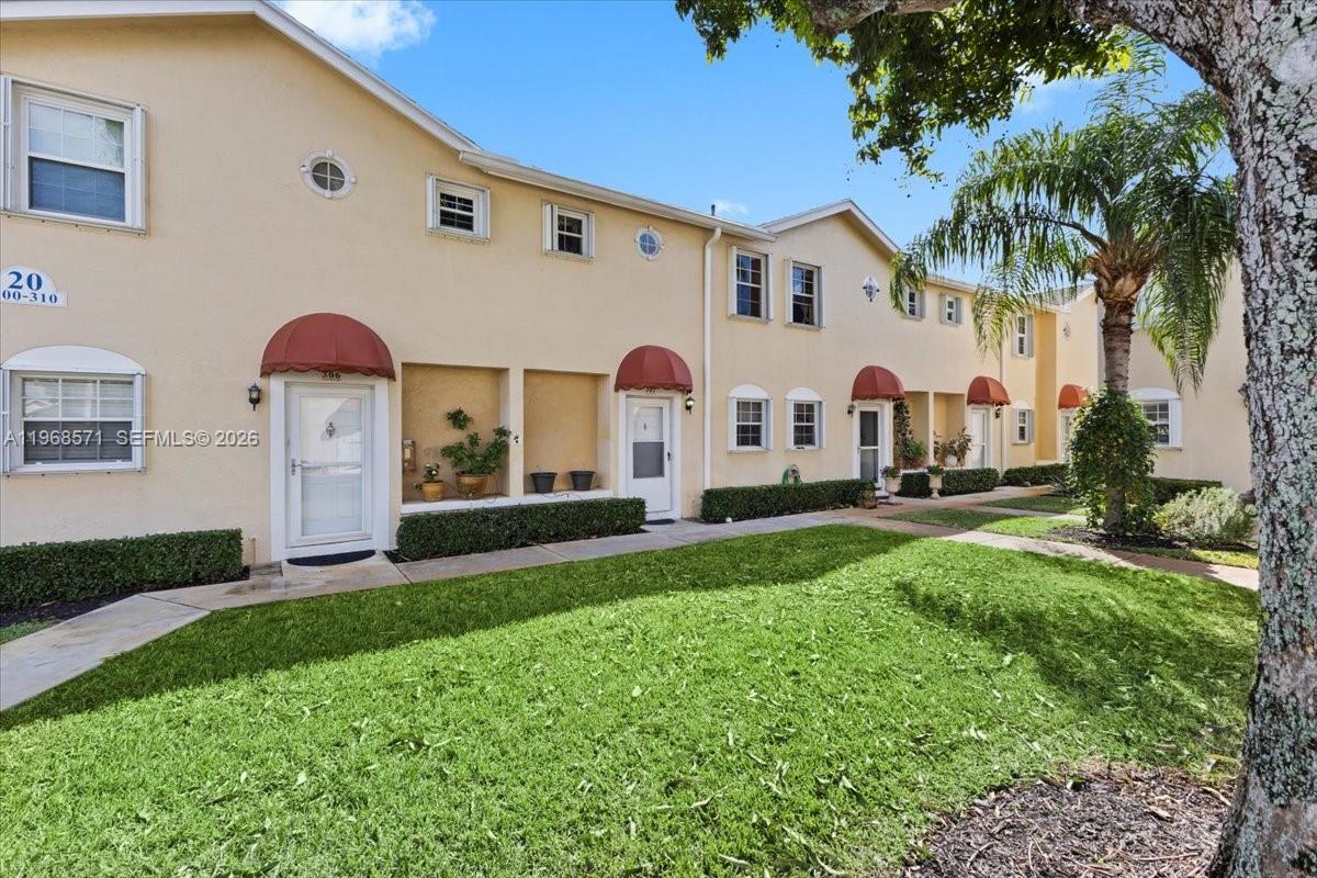 A row of two-story townhomes features beige stucco walls, red awnings, and a grassy lawn — 307 Waterside Dr, Hypoluxo FL 33462, HYPOLUXO, FL