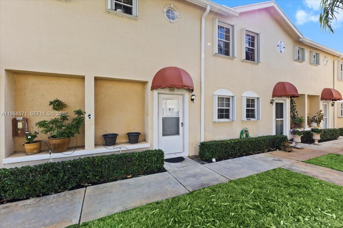 The exterior of a two-story townhouse features beige stucco walls, red awnings, and a walkway — 307 Waterside Dr, Hypoluxo FL 33462, HYPOLUXO, FL