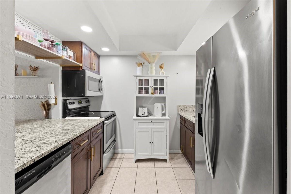 A galley-style kitchen features dark wood cabinets, granite countertops, and stainless steel appliances — 307 Waterside Dr, Hypoluxo FL 33462, HYPOLUXO, FL