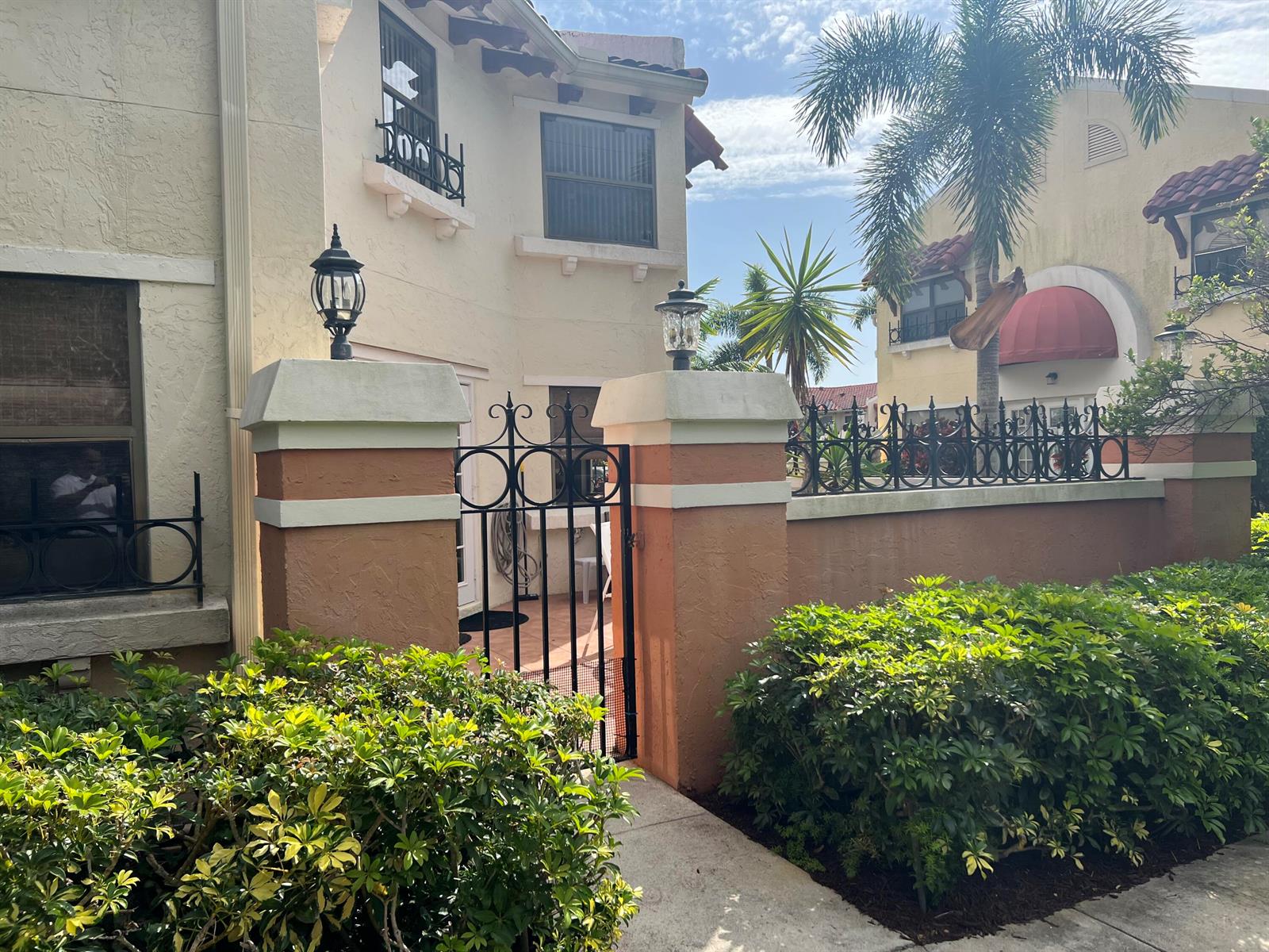 A stucco house exterior features a gated courtyard entrance with decorative metal fencing and lanterns — 13 Uno Lago Drive, Juno Beach FL 33408, JUNO BEACH, FL