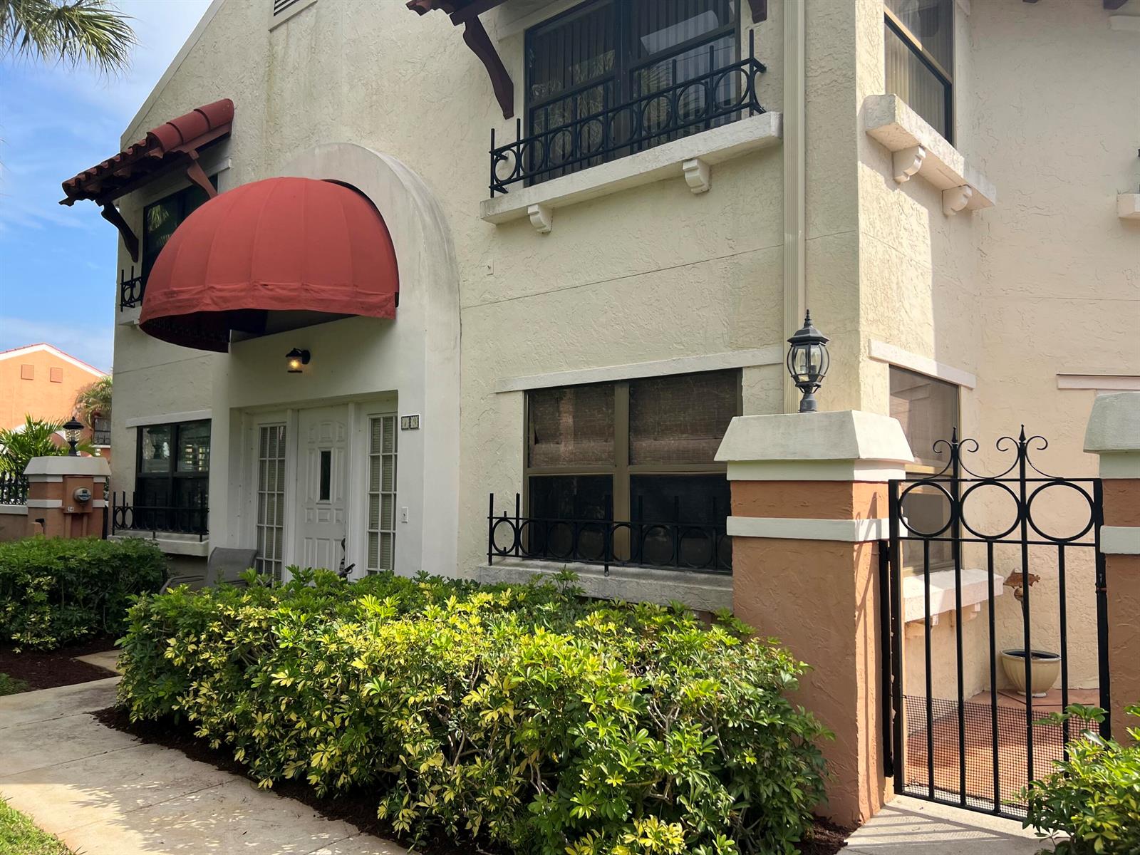 A two-story stucco building features a red dome awning, black iron railings, and landscaping — 13 Uno Lago Drive, Juno Beach FL 33408, JUNO BEACH, FL