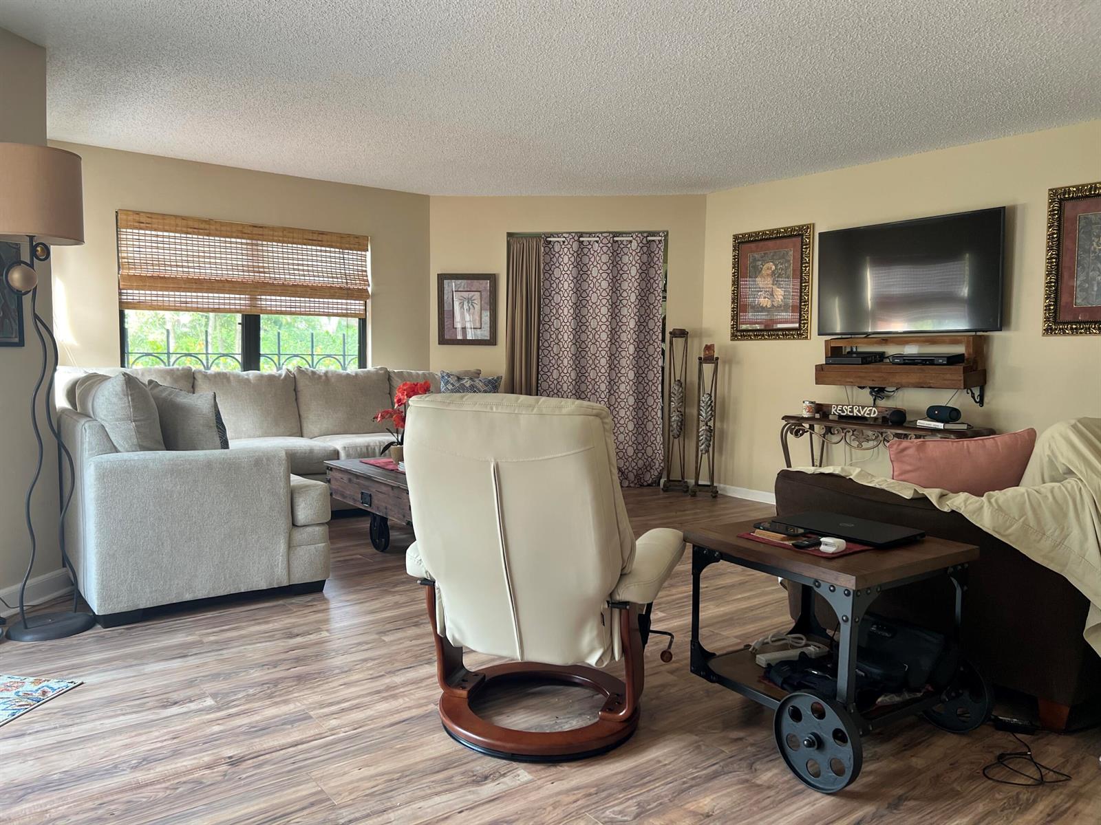 A living room features a sectional sofa, a recliner, a television, and wood-look flooring — 13 Uno Lago Drive, Juno Beach FL 33408, JUNO BEACH, FL
