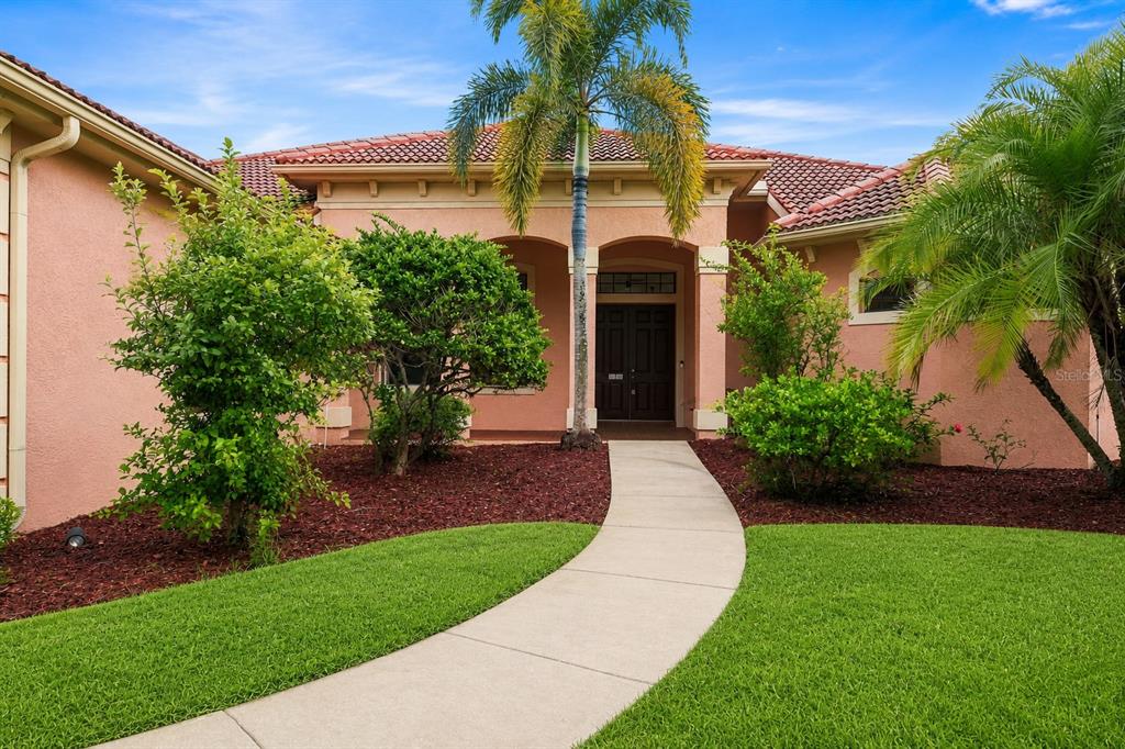 A peach-colored house with a red tile roof, palm trees, and a curved concrete walkway — 10609 CHEVAL PLACE, BRADENTON, FL