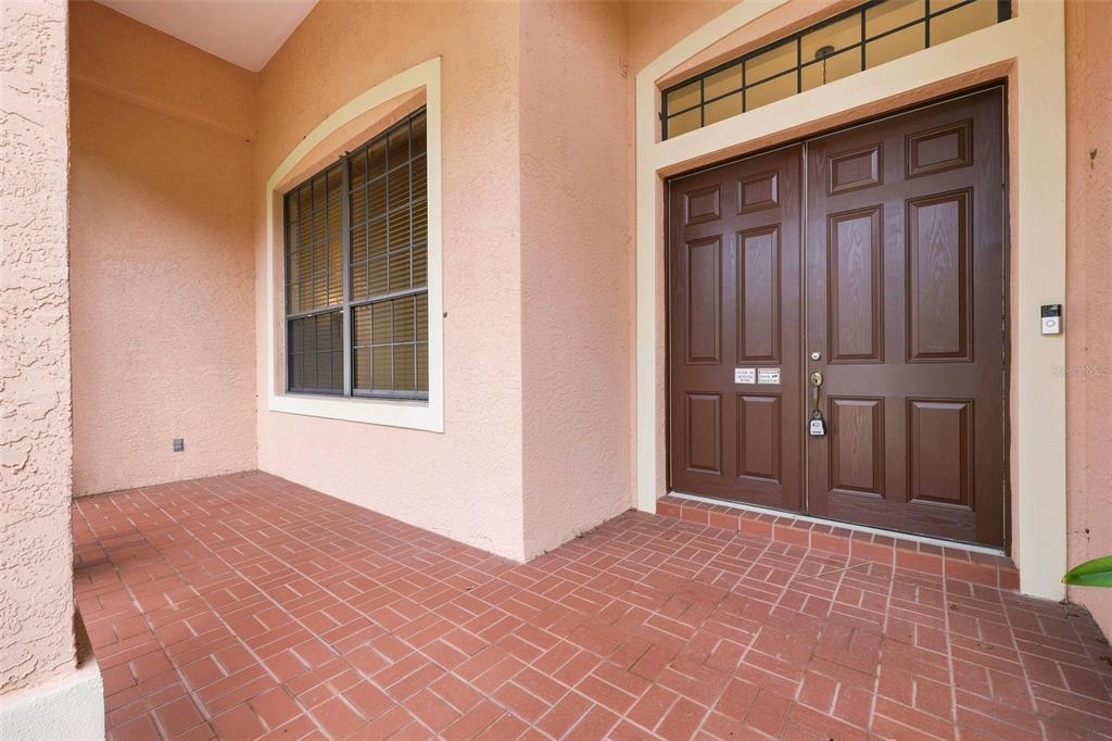 A covered entryway features a red brick floor, a large window, and double brown doors — 10609 CHEVAL PLACE, BRADENTON, FL