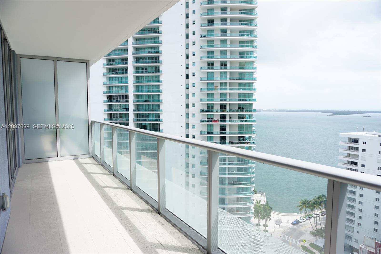A balcony with tiled flooring and a glass railing overlooks a street and the ocean — 1300 Brickell Bay Dr # 1904, Miami FL 33131, MIAMI, FL