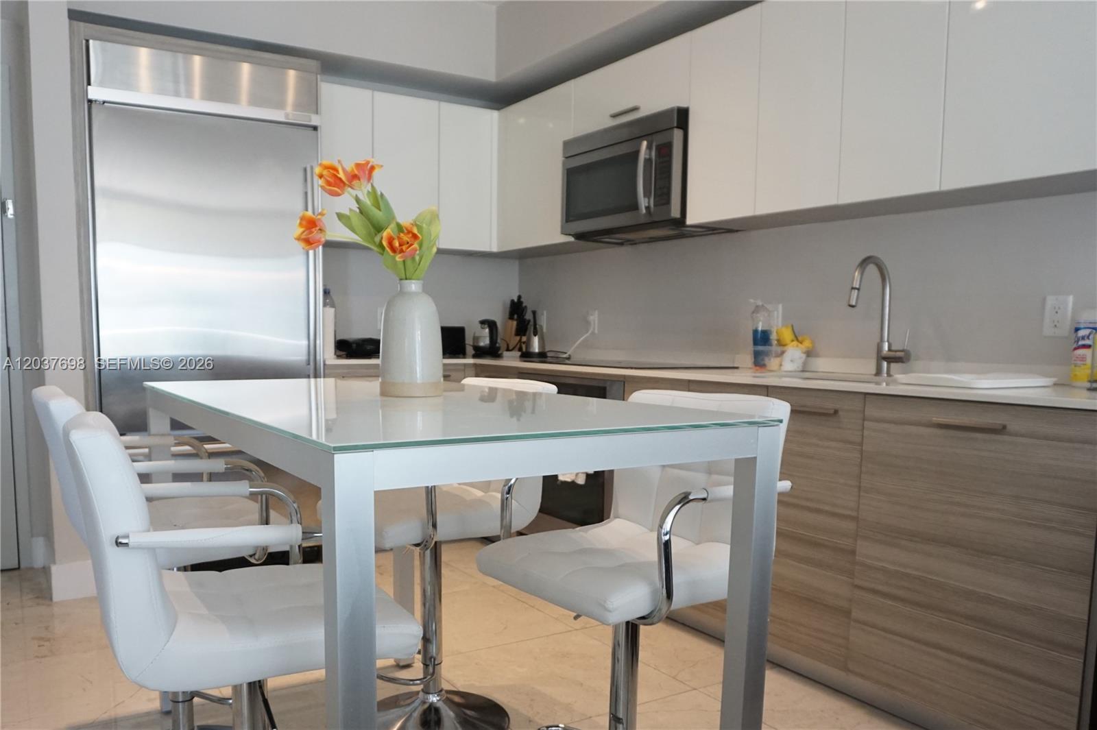 A modern open-concept kitchen and living area features light wood cabinetry, white countertops, and balcony views — 1300 Brickell Bay Dr # 1904, Miami FL 33131, MIAMI, FL