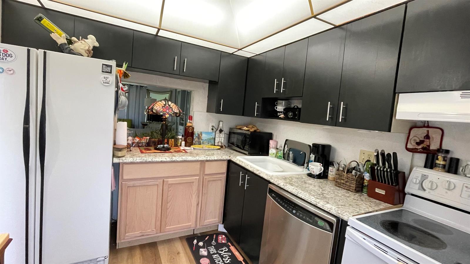A kitchen features black upper cabinets, light wood lower cabinets, and speckled laminate countertops — 4 Abbey Lane # 103, Delray Beach FL 33446, DELRAY BEACH, FL