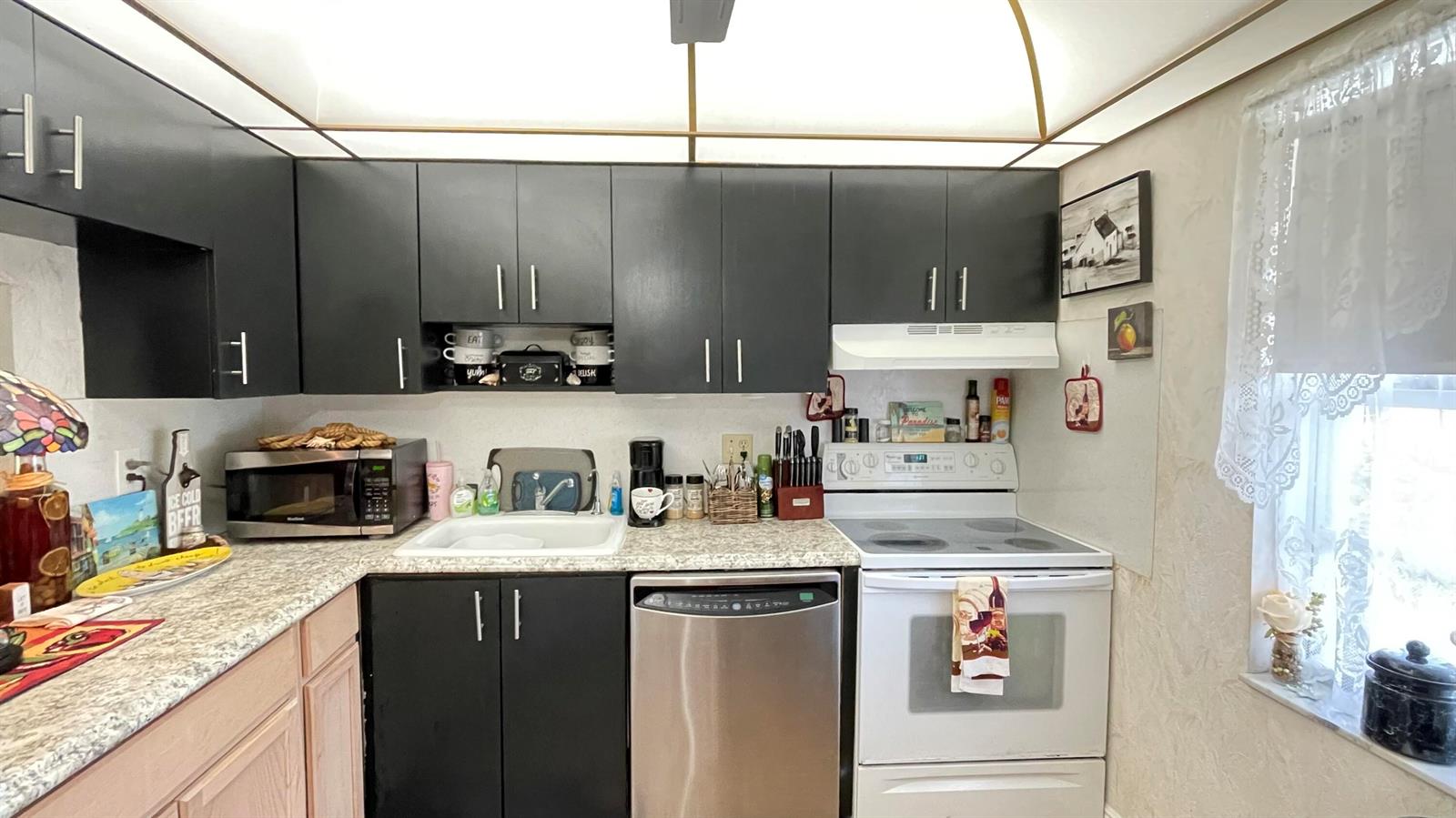 A kitchen features black upper cabinets, a stainless steel dishwasher, and a white electric range — 4 Abbey Lane # 103, Delray Beach FL 33446, DELRAY BEACH, FL