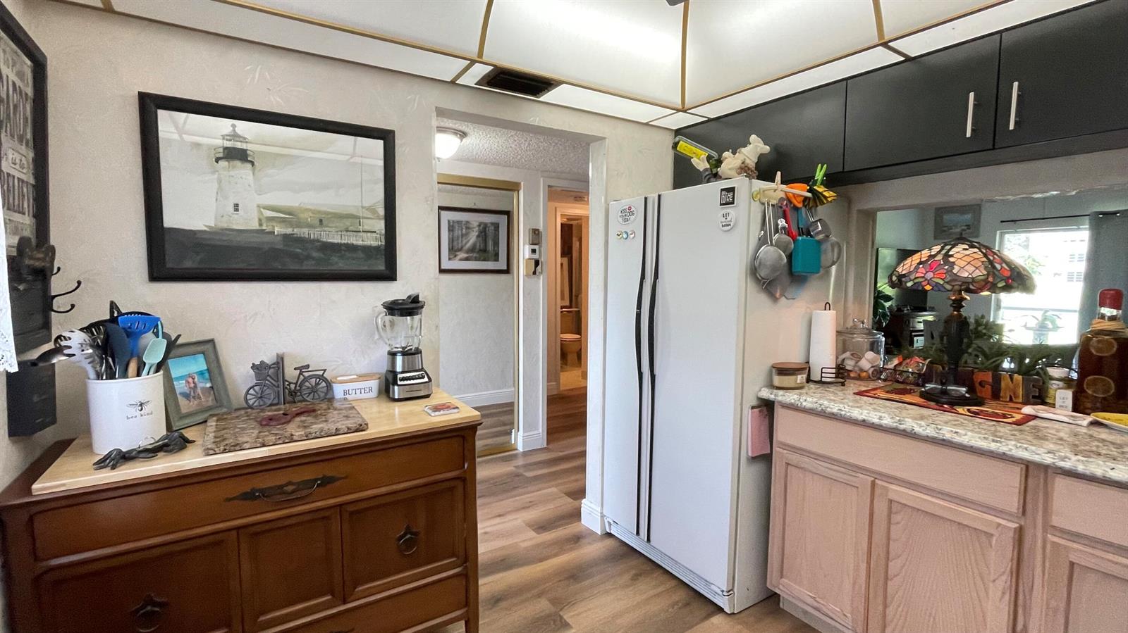 A kitchen features a wooden sideboard, a white refrigerator, and light-colored cabinetry with granite countertops — 4 Abbey Lane # 103, Delray Beach FL 33446, DELRAY BEACH, FL