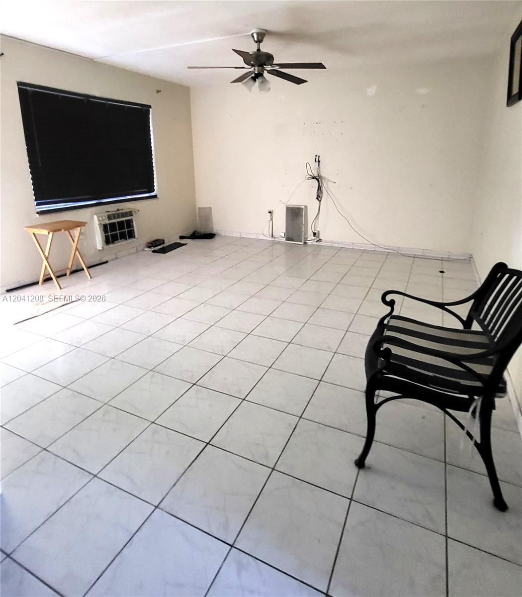 An empty room features white tiled floors, a ceiling fan, and a window air conditioner — 17050 NE 14th Ave # 107, Miami FL 33162, MIAMI, FL