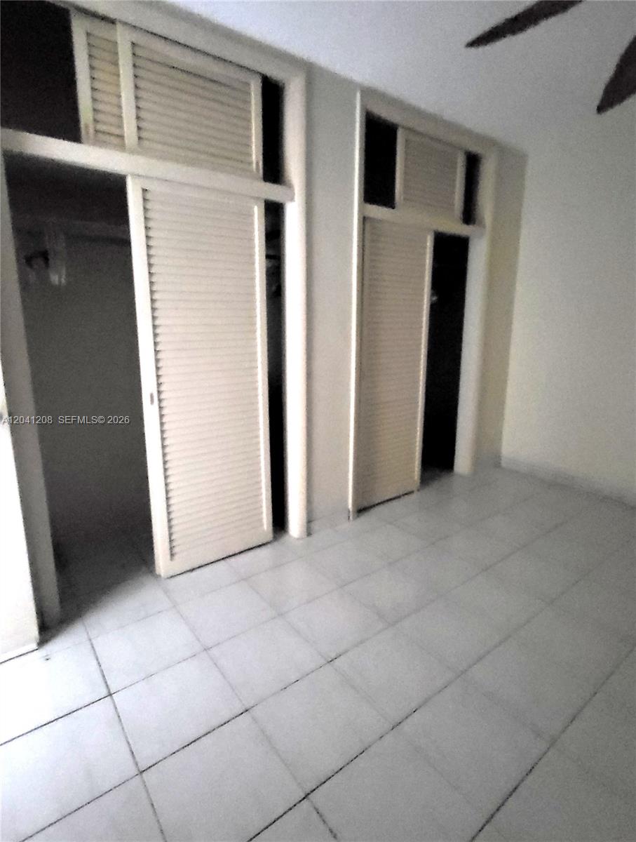 A room with white tiled floors and two sets of louvered closet doors — 17050 NE 14th Ave # 107, Miami FL 33162, MIAMI, FL