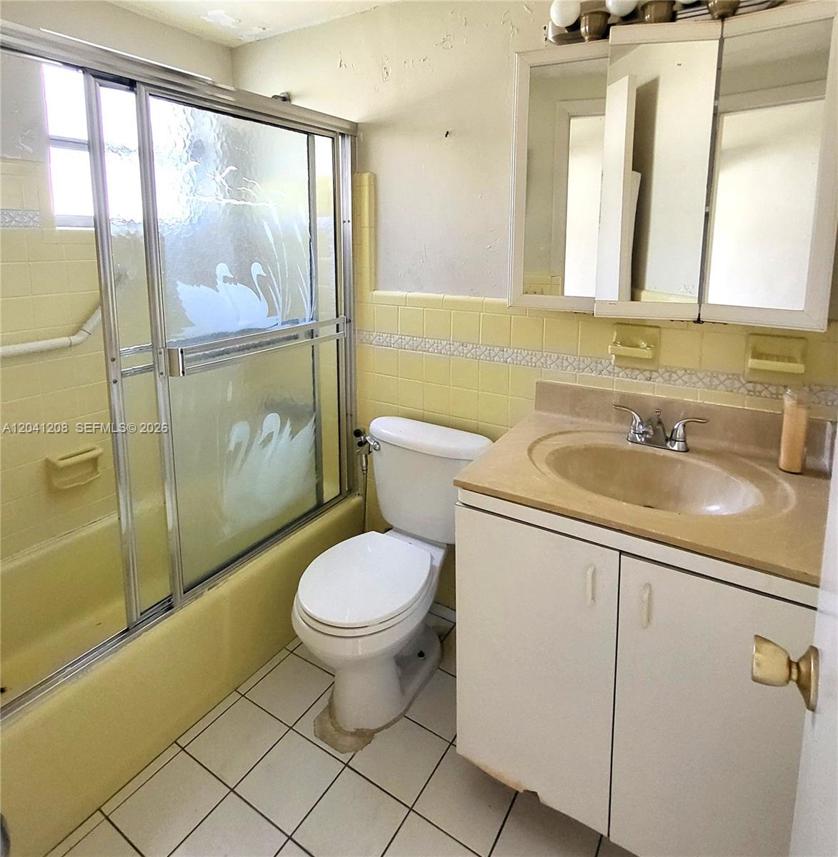 A bathroom features a yellow tiled tub surround, a white toilet, and a vanity cabinet — 17050 NE 14th Ave # 107, Miami FL 33162, MIAMI, FL