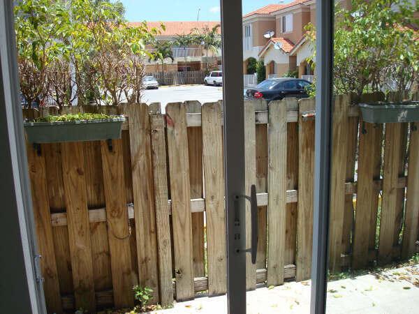 A view through a sliding glass door shows a wooden fence, plants, and parked cars — 229 E 3rd Street # 2, Hialeah FL 33010, HIALEAH, FL