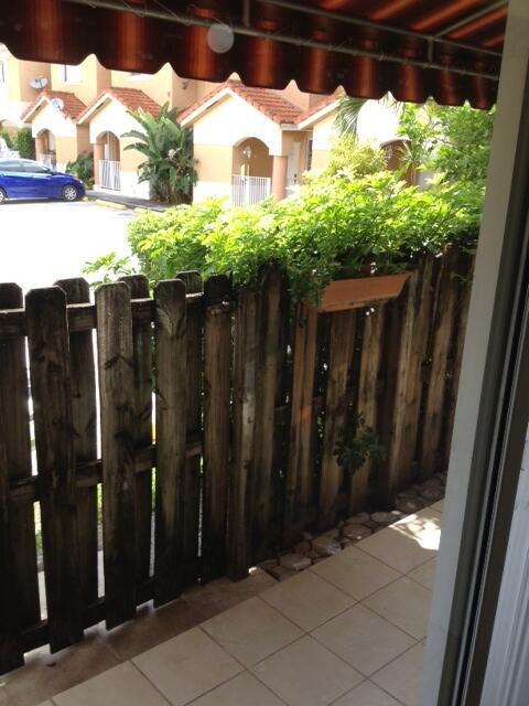 A wooden fence separates a tiled patio from a green hedge and residential buildings — 229 E 3rd Street # 2, Hialeah FL 33010, HIALEAH, FL