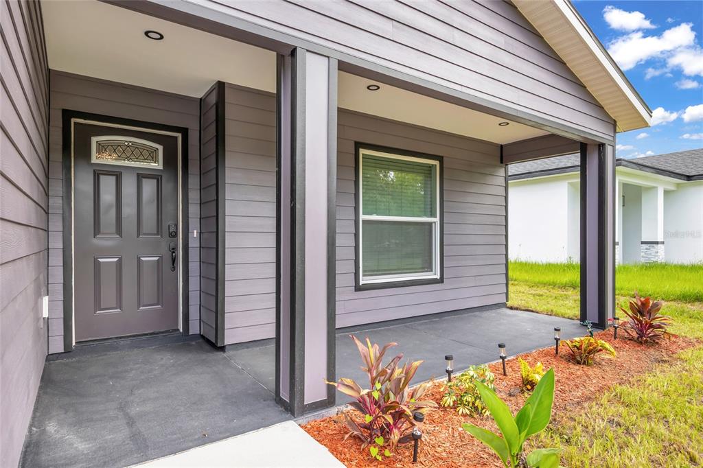 A covered front porch with a gray door, window, and landscaping in front of a house — 1765 ROSEBERRY LANE, SANFORD, FL