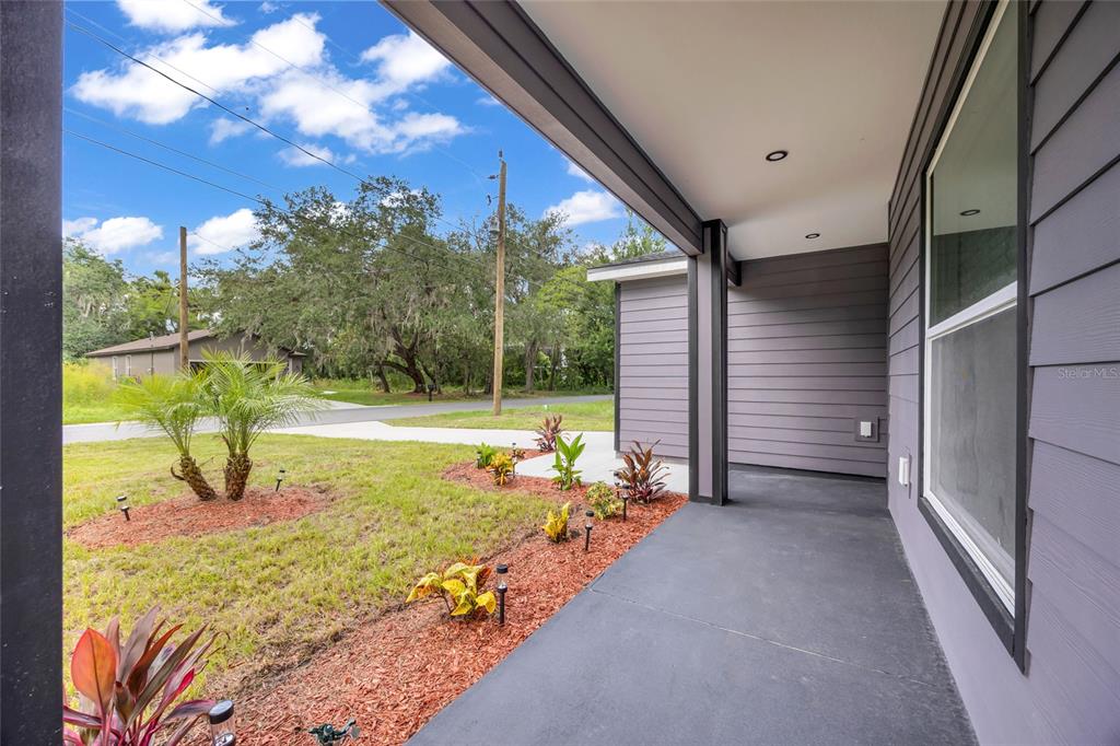 A covered front porch with dark gray siding and concrete flooring overlooks a grassy yard — 1765 ROSEBERRY LANE, SANFORD, FL