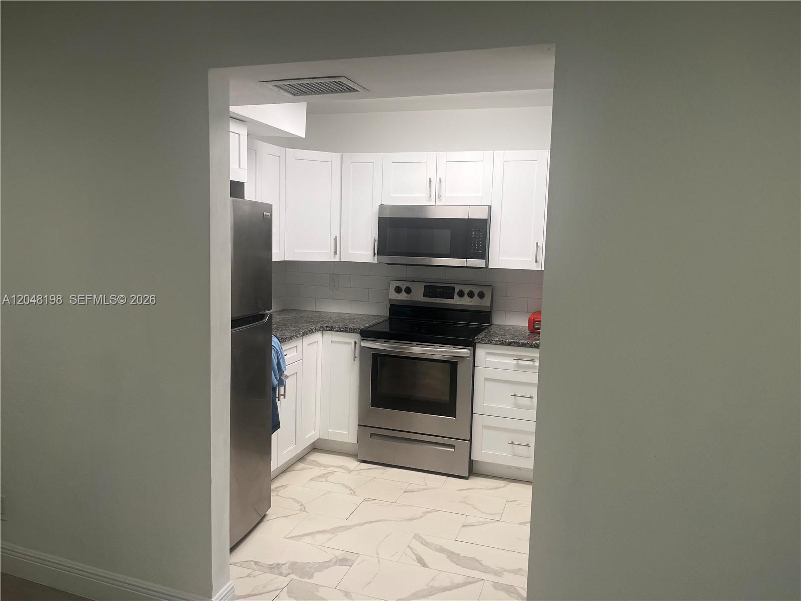 A kitchen features white cabinets, stainless steel appliances, granite countertops, and light-colored tile flooring — 5952 NW 25th Pl # 234, Sunrise FL 33313, SUNRISE, FL