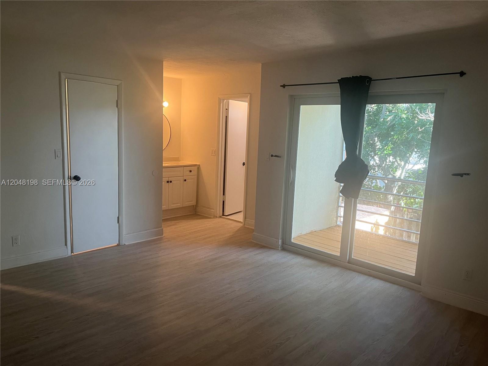 A bedroom with light wood-look flooring, a bathroom vanity area, and a sliding glass balcony door — 5952 NW 25th Pl # 234, Sunrise FL 33313, SUNRISE, FL
